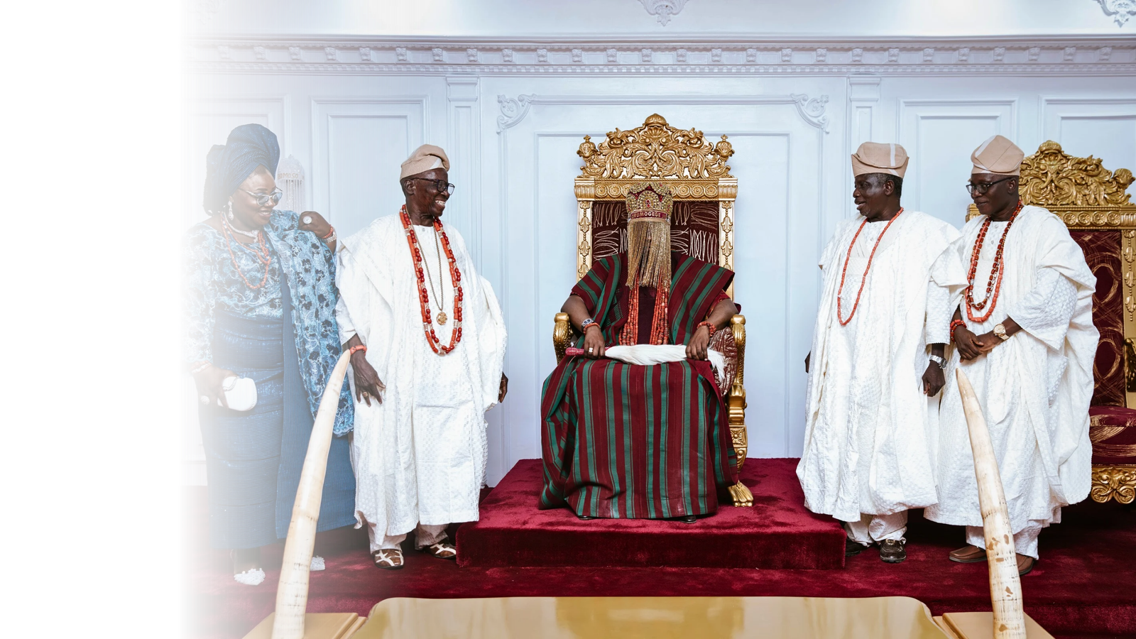 Oba Ghandi Olaoye seated on an ornate gold throne with palace figures standing beside him.